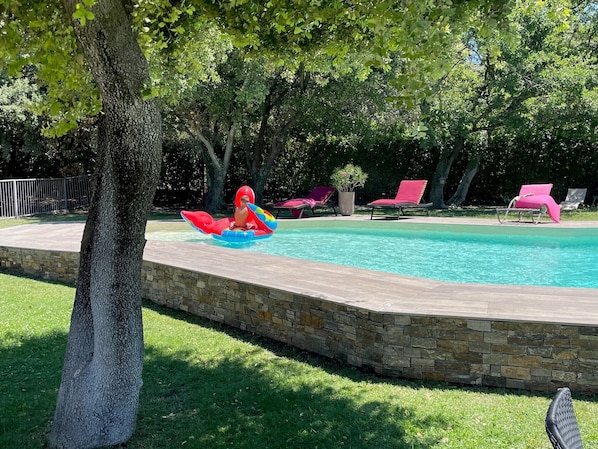 A swimming pool with a stone border, surrounded by grass and trees.