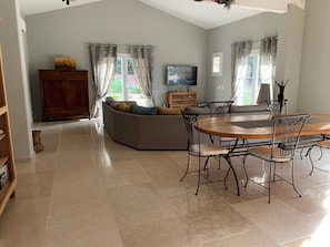 A spacious living room with a large sofa, a dining table with chairs, a television, and a wooden cabinet.