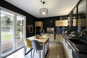 A modern kitchen with a dining area, large windows, and a view of the outdoors.