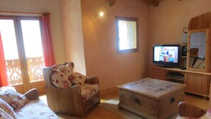 Ein gemütliches Wohnzimmer mit einer Holzdavonia, einem Holzsesselsowie einem Couchtisch aus Holz, einem Fernseher und einem Holzschrank.