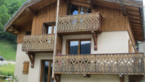 Eine zweistöckige Holzchalet mit Balkonen, großen Fenstern und einer Bergkulisse im Hintergrund.