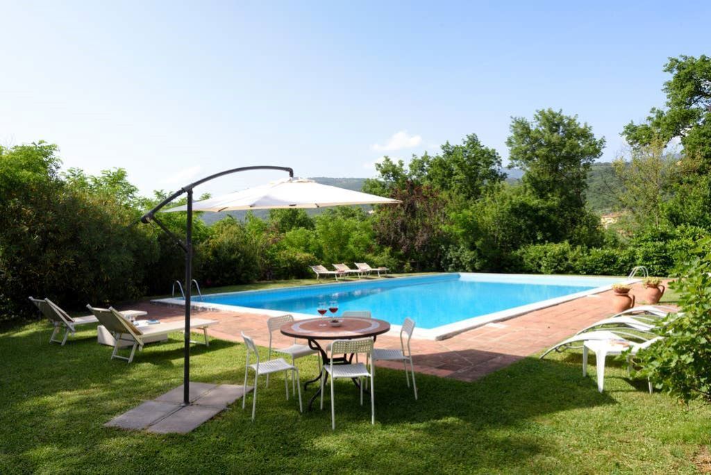 A rectangular swimming pool with a tiled deck, surrounded by a grassy area with lounge chairs and a table.