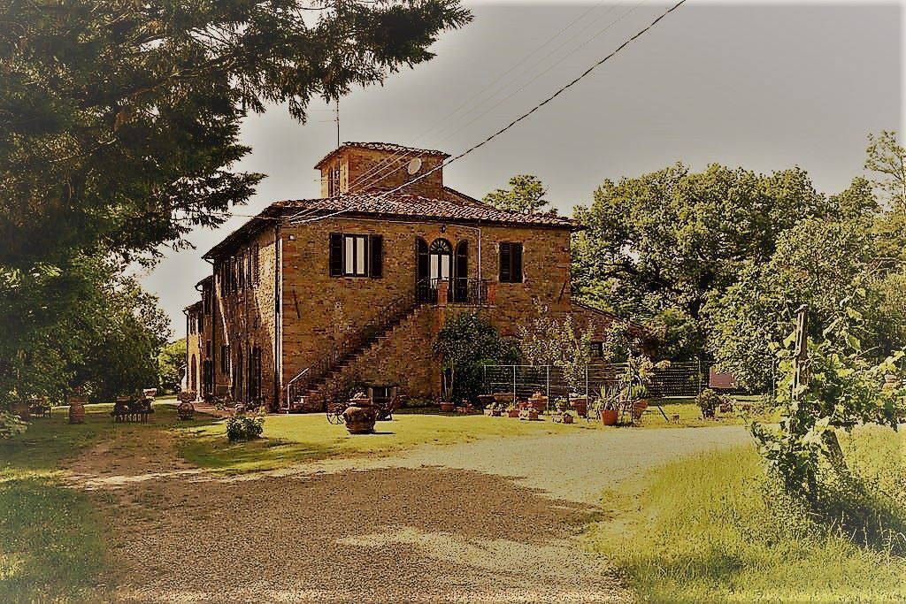 A rustic stone building with a chimney, a staircase, and a paved driveway.