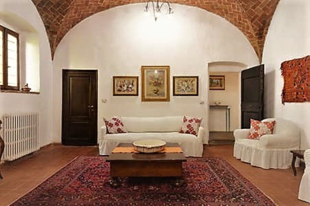 A cozy living room with a white sofa, a coffee table, and a patterned rug. There are framed pictures on the wall and a fireplace in the background.