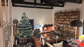 Ein gemütliches Wohnzimmer mit einem großen Weihnachtsbaum, einem Kamin, einer Bücherwand und einem Essbereich.