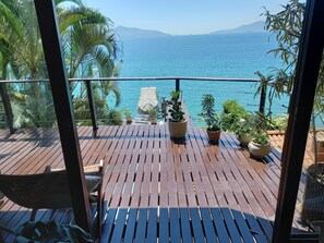 Una terraza de madera con plantas en macetas y vistas al mar.