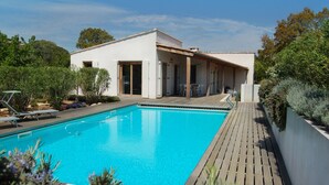 Ein modernes Haus mit Swimmingpool, Holzterrasse und überdachter Terrasse.