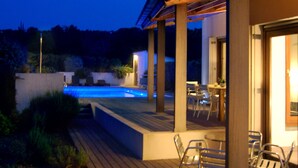 Eine Holzterrasse mit Pool, Gartenmöbeln und einer überdachten Veranda.