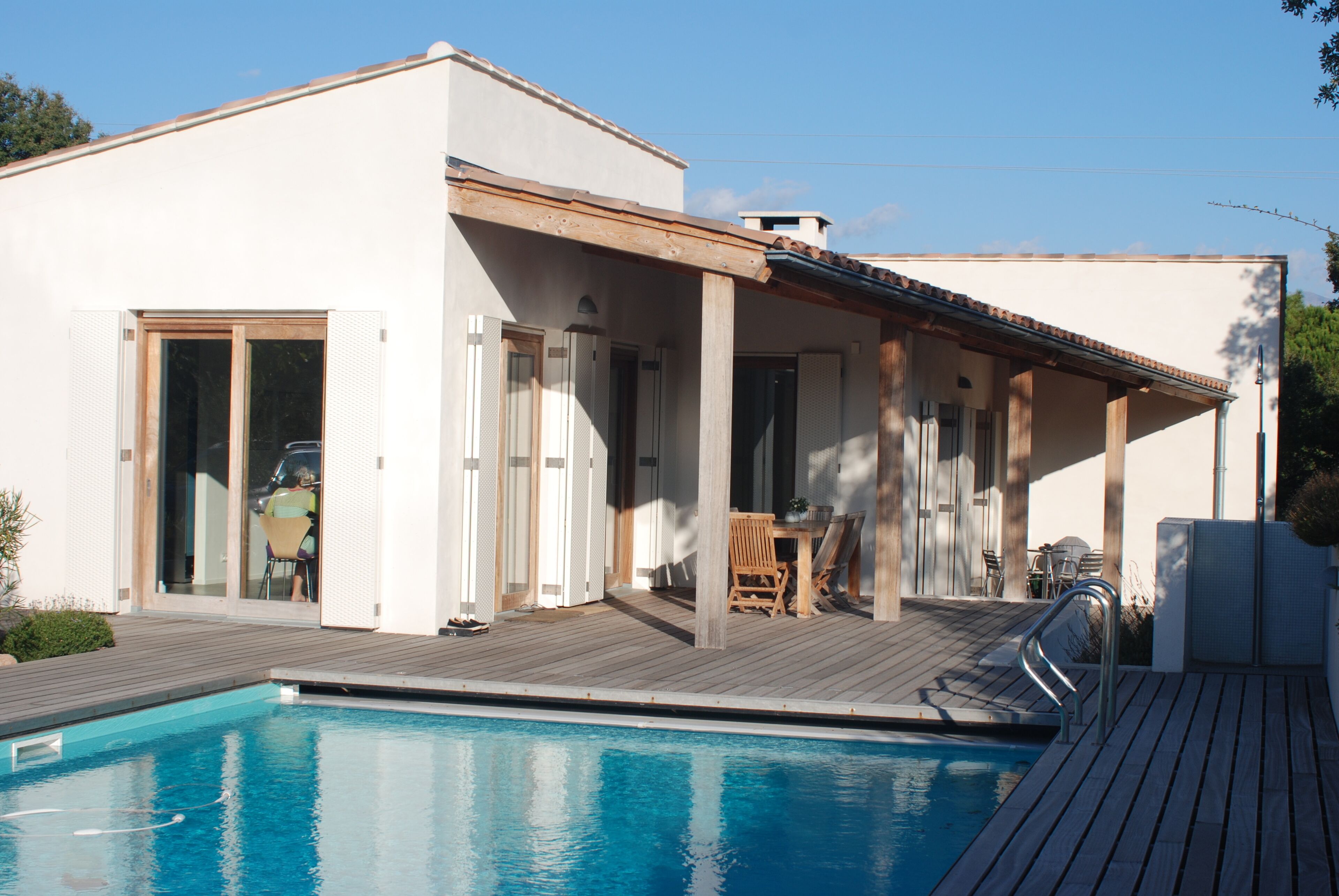 Een modern huis met zwembad, houten terras en een overdekte patio.