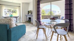 Een moderne woonkamer met een bank, een glazen tafel met stoelen, een open haard en een balkon met gordijnen.