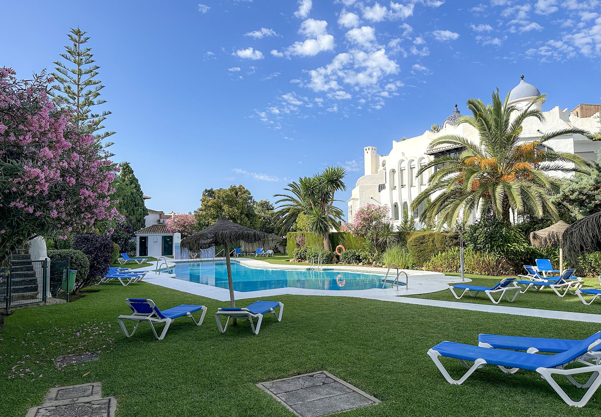 A pool area with blue lounge chairs, a clear blue sky, and a white building with a dome.
