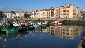A marina with boats docked, a stone wall, and buildings with red and white facades in the background. - ANGLET T2 Classified - Beaches and Forest, Comfortable, Terrace 25m2, Baby equipment (Anglet)