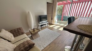 A living room with a sofa, a coffee table, a TV, and a balcony with a red and white striped fence. - ANGLET T2 Classified - Beaches and Forest, Comfortable, Terrace 25m2, Baby equipment (Anglet)