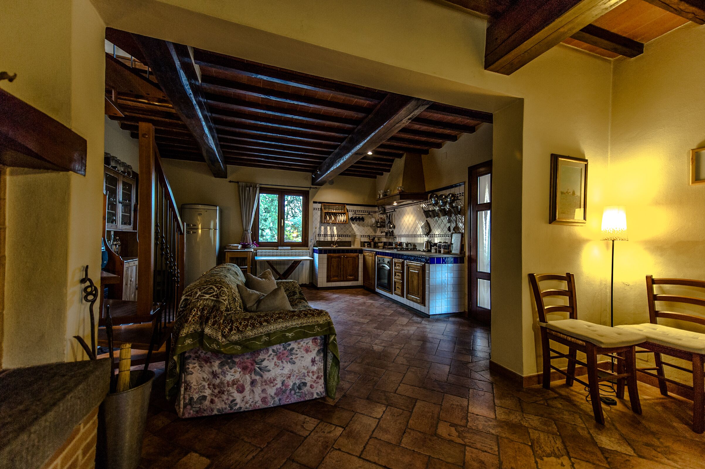 A spacious living area with a sofa, wooden chairs, a kitchen in the background, and a staircase leading upstairs.