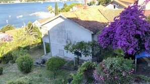 Un bâtiment situé sur la côte, doté d’une façade blanche, d’un toit en tuiles et d’un jardin agrémenté de fleurs violettes.