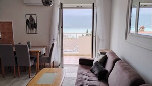 Un salon moderne avec un canapé, une table à manger et des chaises. Il y a une grande fenêtre donnant sur la mer et un balcon.