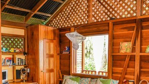 A cozy cabin-style room with a bed, a desk, and a window overlooking greenery. - Casa Del Caribe with Bali Style Pool for Rent in Cocles, 300 meters from beach (Cocles)