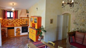 Een gezellige woonkamer met een eethoek, een keuken met zwart-witte vloertegels en een stenen muur.