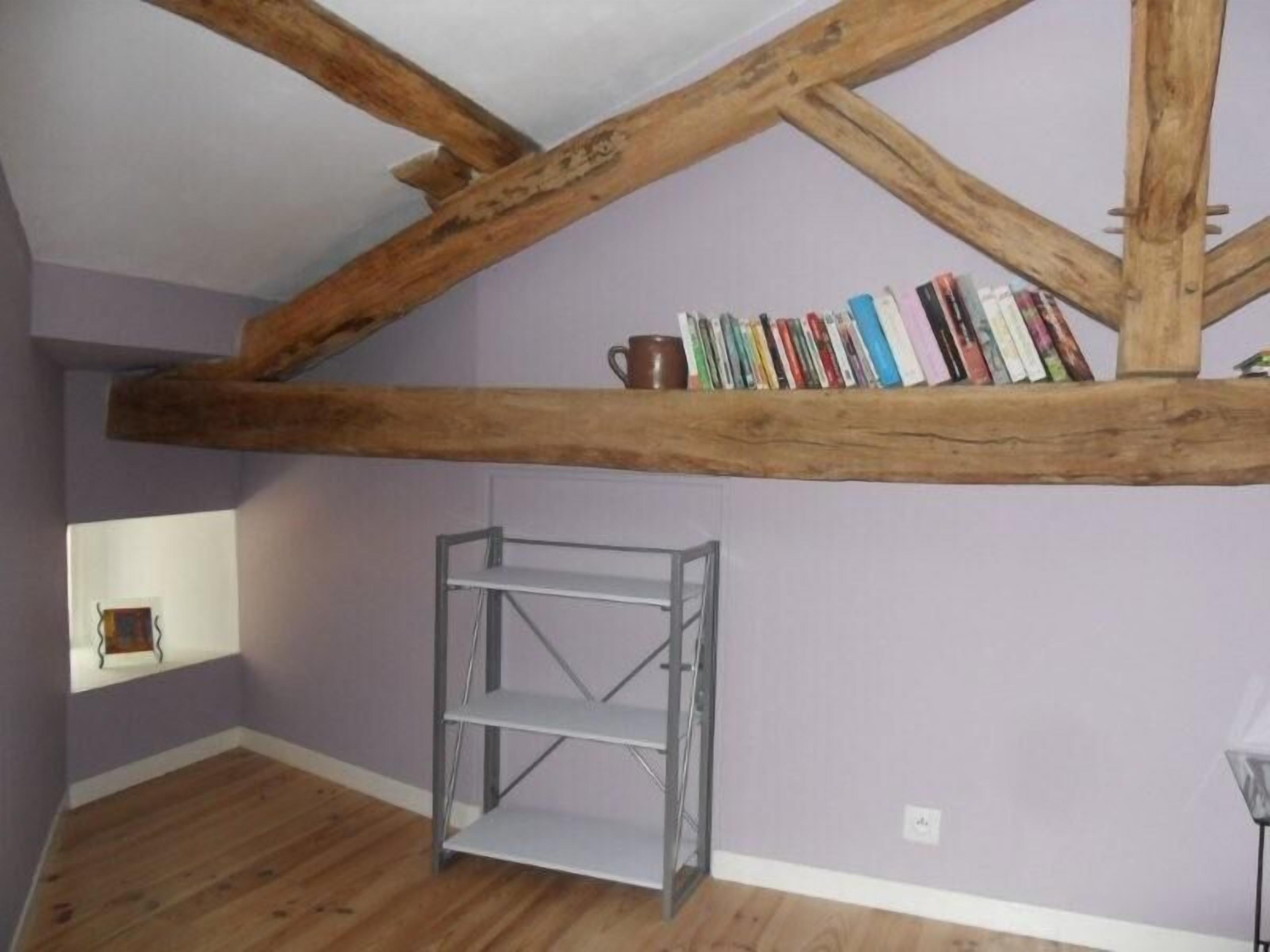 A room with a sloped ceiling supported by wooden beams, a metal shelf unit, and a window with a view of the outside.