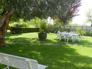 A well-maintained garden with a lawn, a large planter with plants, and a white plastic table and chairs set up for outdoor dining. - Gîte120m2,3étoiles closed park 4000m2,(86) FUTUROSCOPE 40min (Saint-Secondin)