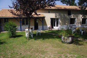 A house with a tiled roof, a covered patio with plastic chairs, and a garden area with a small tree and a potted plant. - Gîte120m2,3étoiles closed park 4000m2,(86) FUTUROSCOPE 40min (Saint-Secondin)