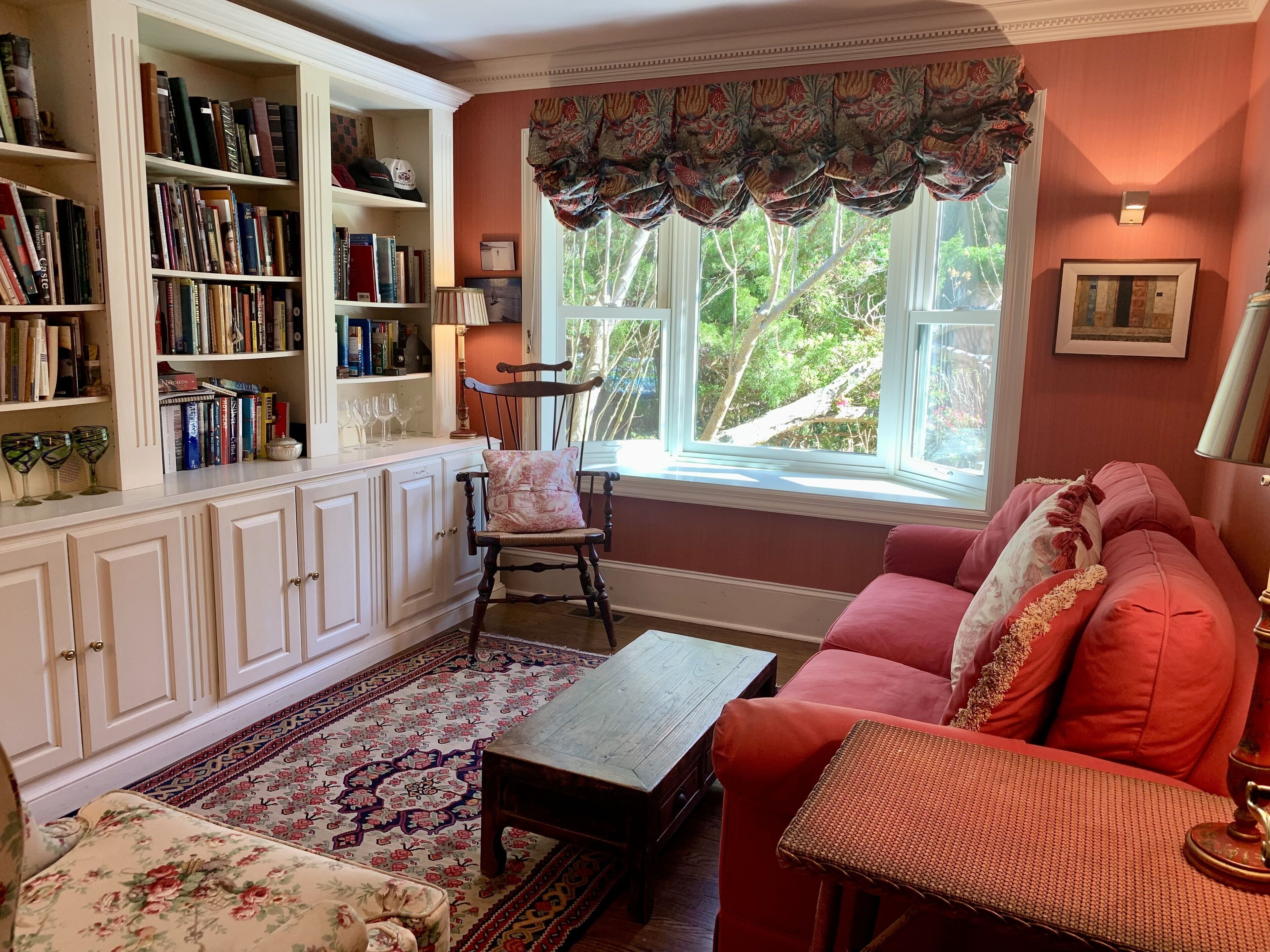 Un salon chaleureux avec une bibliothèque, un canapé rouge, une table basse en bois et un tapis à motifs.