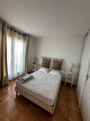 Une chambre à coucher avec un lit, des rideaux, une table de chevet avec une lampe et une commode.