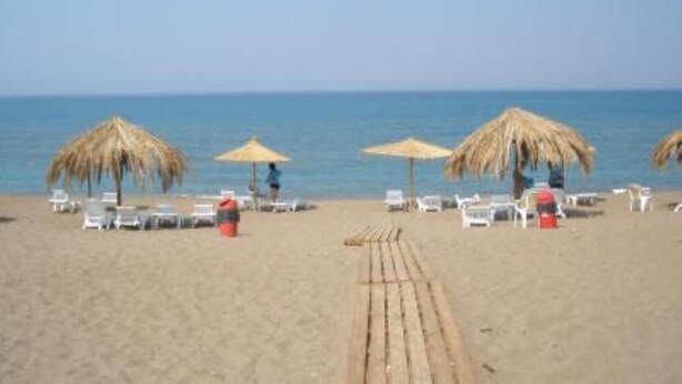 A beach with thatched umbrellas, white lounge chairs, and a wooden walkway leading to the water.