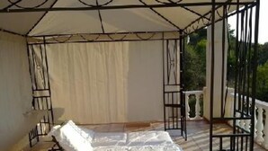 A covered outdoor seating area with a cushioned bench, a table, and a railing.