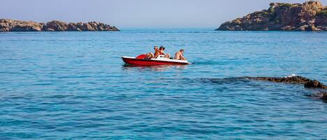 A small red boat with people on a calm sea, rocky islands in the background.