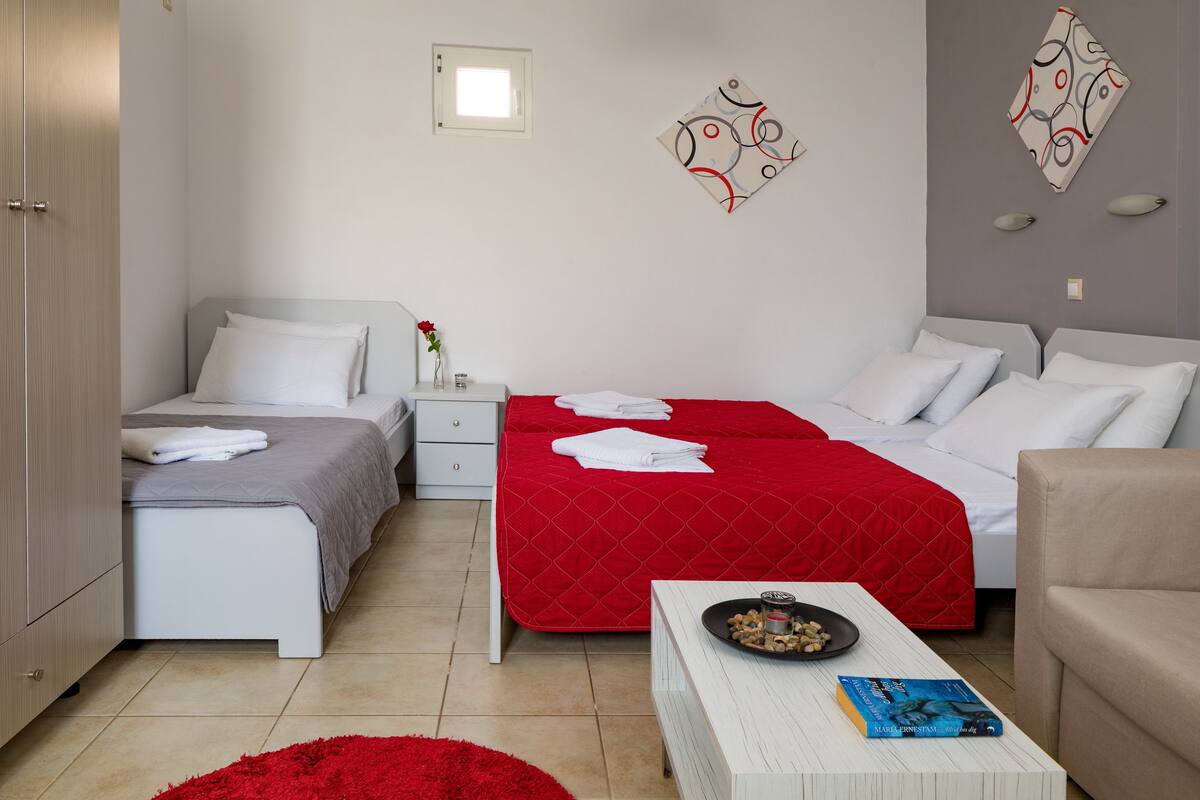 A modern hotel room with two beds, a red and white bedspread, a white bedside table with a book, a red rug, and a wall art piece.