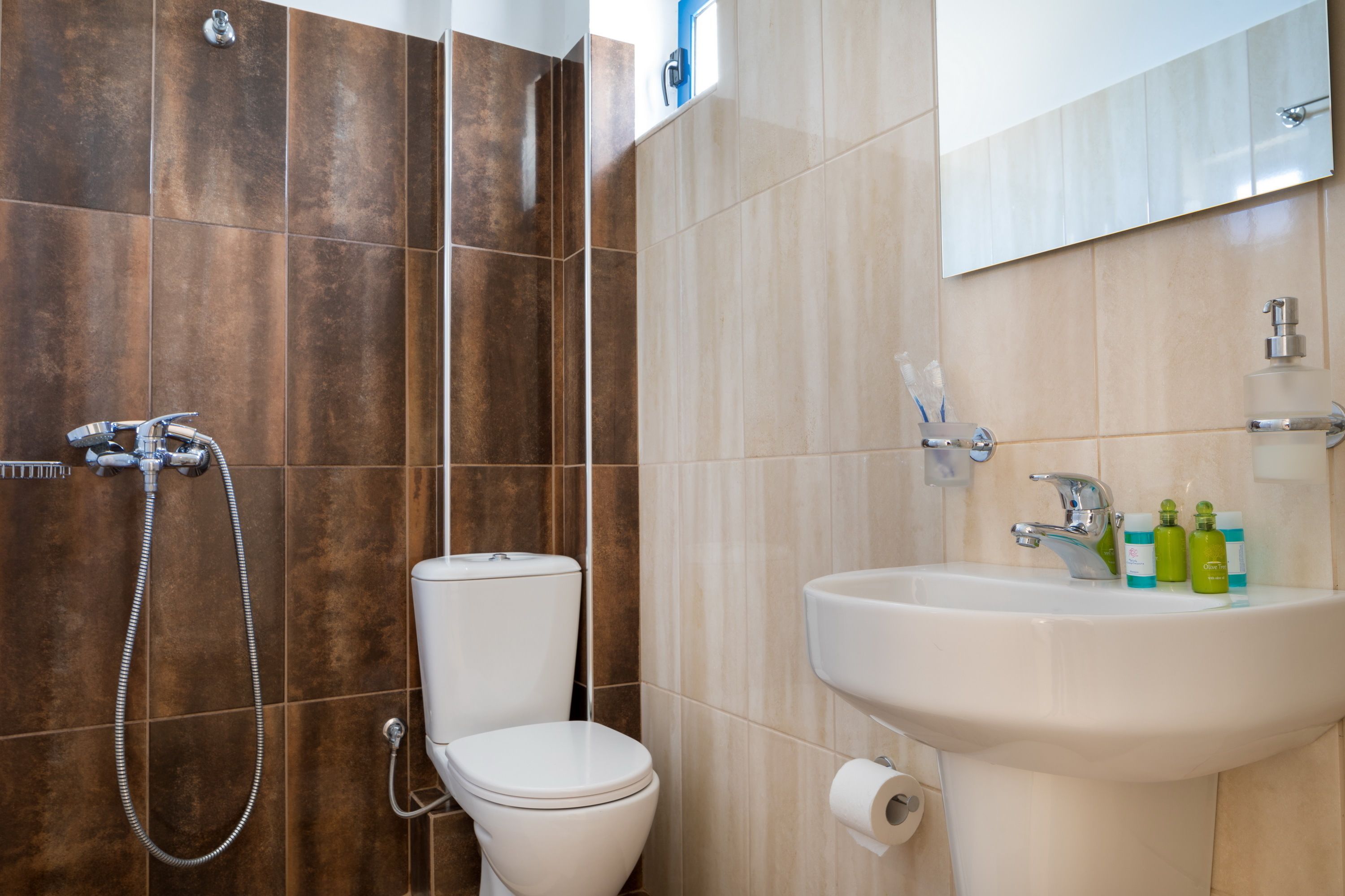 A bathroom with a toilet, shower, sink, and mirror.