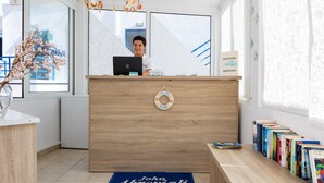 A reception desk with a laptop, a welcome board, and a blue mat indicating John Aerovali rooms. - John Akroyiali rooms (Sfakia)