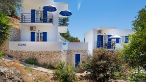 A building with a stone facade, blue shutters, and a sign labeled "ROOMS". - John Akroyiali rooms (Sfakia)