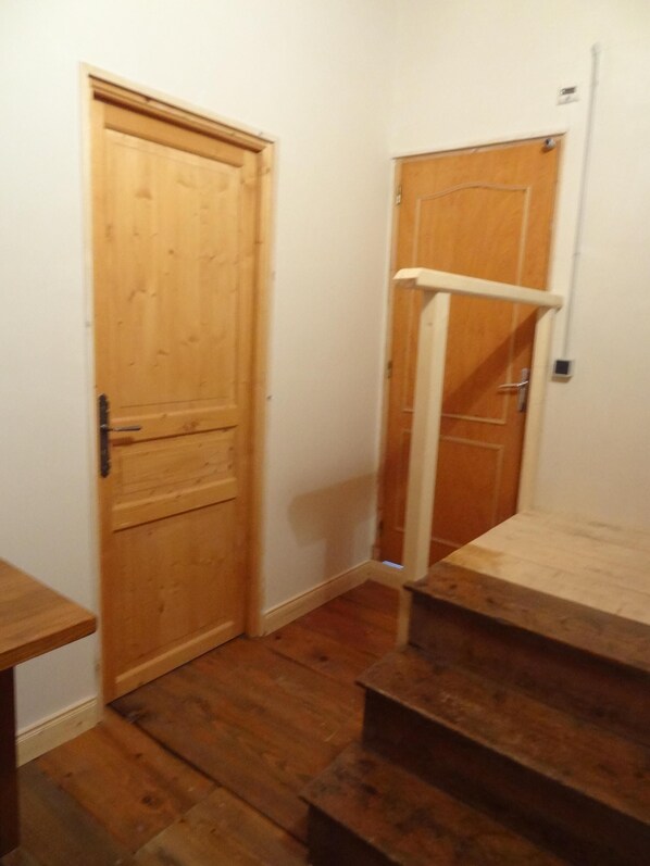A wooden door with a metal handle, a white wall, and a wooden staircase.