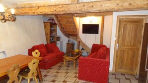 A cozy living room with a wooden ceiling, a dining table with chairs, and two red sofas. - Perfect  location quiet surroundings  spacious comfortable & functional  (Brides-Les-Bains)