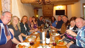 A group of people seated around a wooden dining table with various dishes and drinks, in a room with wooden beams and a chandelier. - Perfect  location quiet surroundings  spacious comfortable & functional  (Brides-Les-Bains)