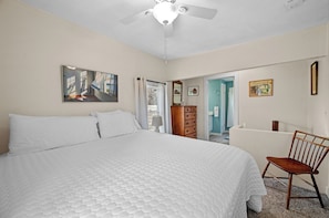 A bedroom with a large bed, a ceiling fan, a wooden dresser, and a chair.