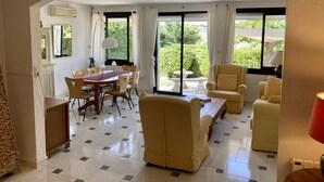 Un vaste espace de vie comprenant une table à manger, des chaises, des canapés et une grande fenêtre donnant sur un paysage verdoyant.