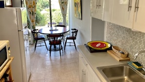Une cuisine moderne avec des meubles blancs, une table de salle à manger ronde entourée de chaises, une grande fenêtre avec des rideaux et un évier avec un égouttoir à vaisselle.
