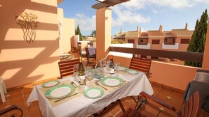 Un área de comedor al aire libre con una mesa preparada para cuatro personas, rodeada de sillas, bajo una pérgola.