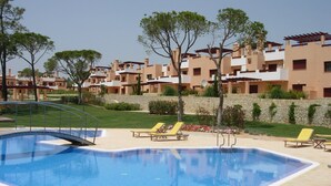 Una piscina con solárium de piedra, rodeada de sillones de descanso y un muro de piedra.