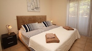 Una cama bien hecha con ropa de cama a rayas, un cabecero y dos almohadas. Hay una mesita de noche con una lámpara y una toalla doblada sobre la cama.