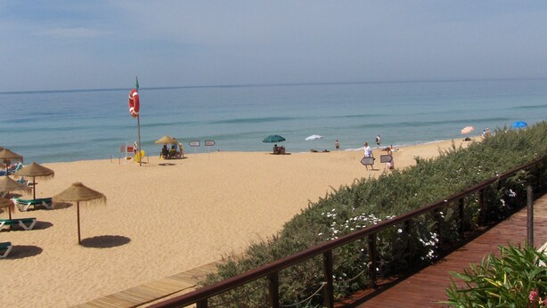 Una playa con sombrillas, sillas reclinables y un camino de madera.