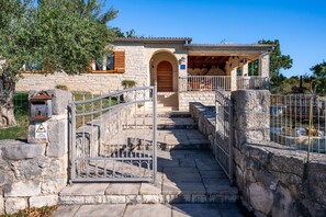 A stone building with a wooden door, a covered porch, and a stone staircase leading to a gated entrance.