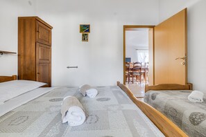 Ein Hotelzimmer mit zwei Betten, einem Holzschrank, einem kleinen Gemälde und einem Essbereich, der durch eine offene Tür sichtbar ist.