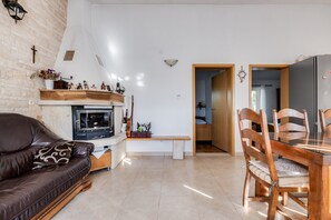 Ein gemütliches Wohnzimmer mit Kamin, eine Essecke mit Holzkästen und eine durchgehende Tür sichtbare Küche.