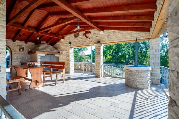An outdoor patio with stone walls, a wooden table, benches, and a stone fountain. - Holiday house Maslina * 2000 m2 garden, private pool, free WiFi (Benkovac)