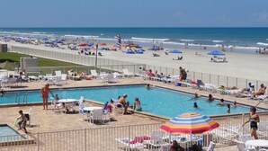 A pool area with multiple lounge chairs and umbrellas, a beach in the background, and a clear sky. - 1 Bdrm..2026 Year-round time slots ..great View & Reviews...on the no drive sand (New Smyrna Beach)