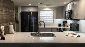 A modern kitchen with stainless steel appliances, a double sink, and a bar area with stools. - 1 Bdrm..2026 Year-round time slots ..great View & Reviews...on the no drive sand (New Smyrna Beach)